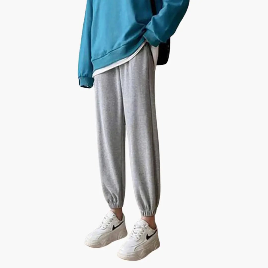 Women's jogging pants with drawstring waistband and cuffed ankles in gray, paired with Nike sneakers.