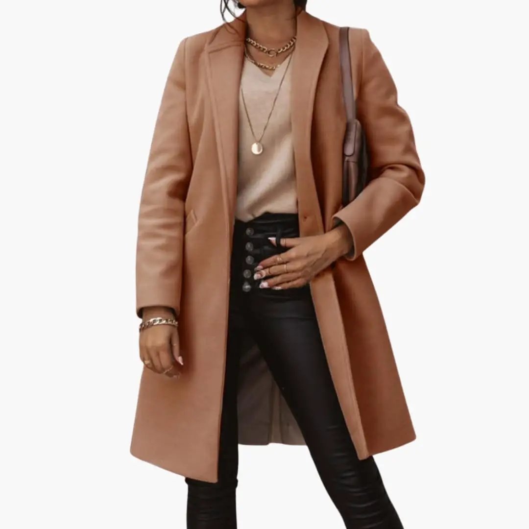 Women's long coat with collar and buttons in camel brown, worn over a beige top and black leather pants.