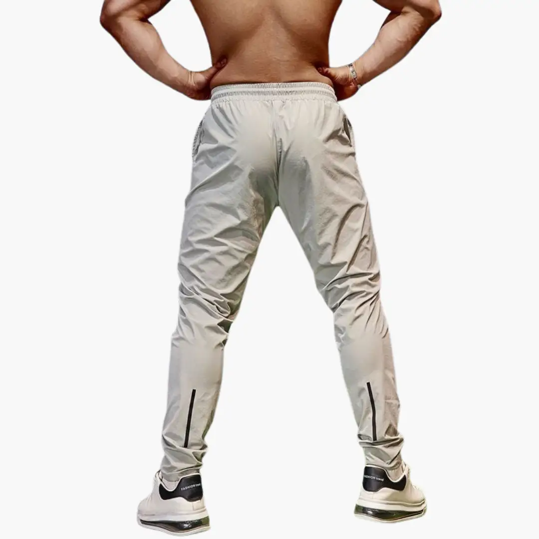 Men's jogging pants with elastic waistband in beige, back view with black ankle zipper accents