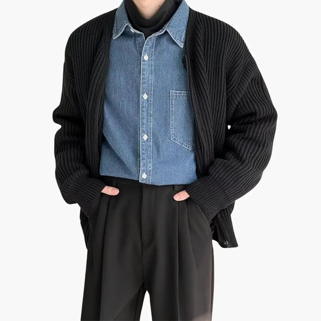 Cardigan for men in black ribbed knit, worn over a blue denim shirt with black trousers.