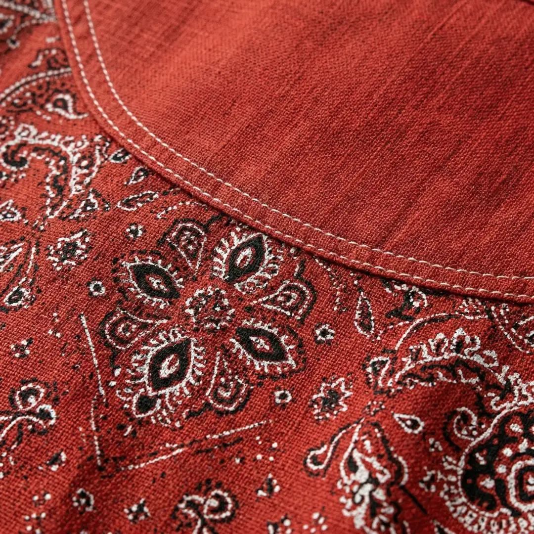Women's button-down shirt in red paisley print with visible white stitching along the collar seam and textured fabric.