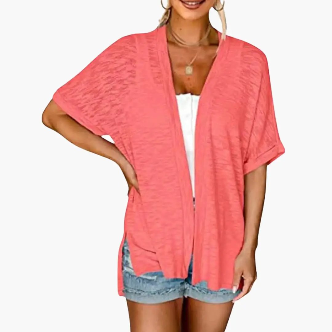 Women's coral pink open-front cardigan with short sleeves, layered over a white top and denim shorts.